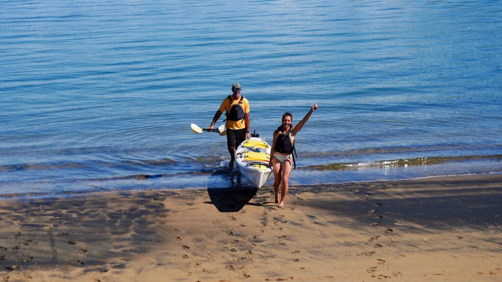 couple walking carrying kayak at tata island tata beach nelson tsman nz